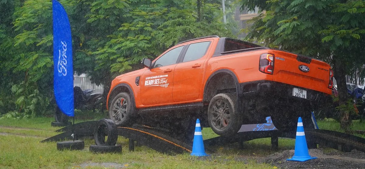 Ford Ranger màu cam leo dốc nghiêng trong bài lái thử sa hình dưới trời mưa
